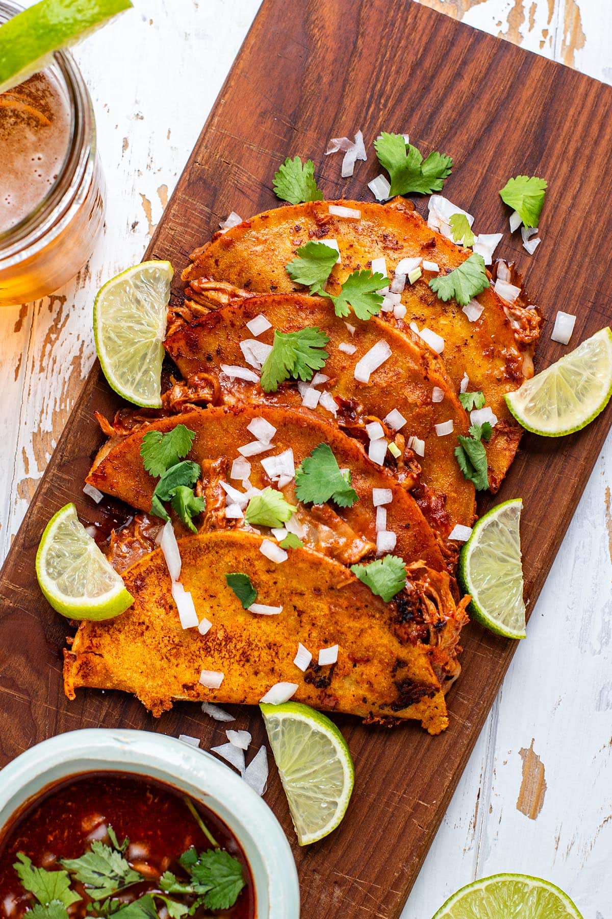 Chicken Birria tacos on a wooden cutting board topped with fresh cilantro and chopped white onion.