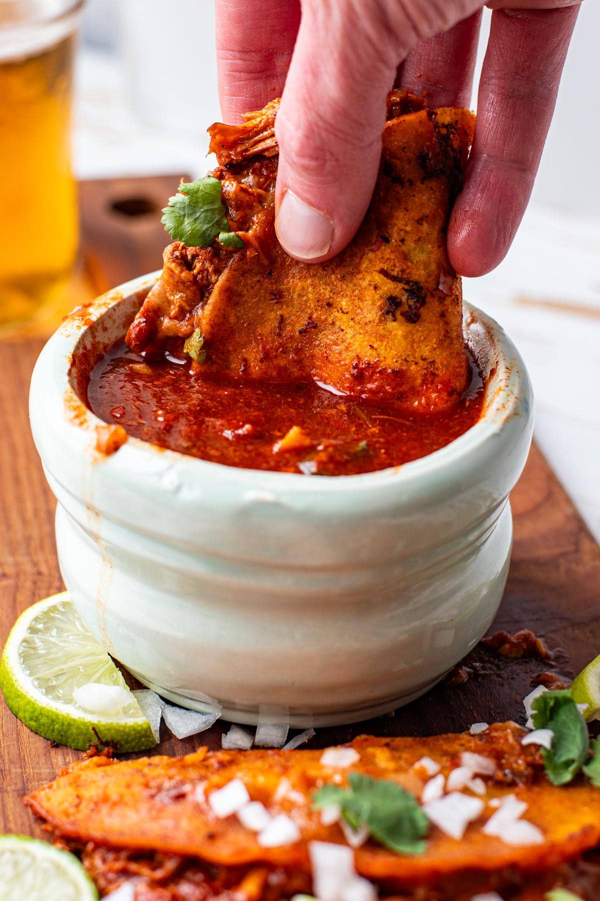 A hand holding a chicken birria taco and dipping it in consomé sauce.