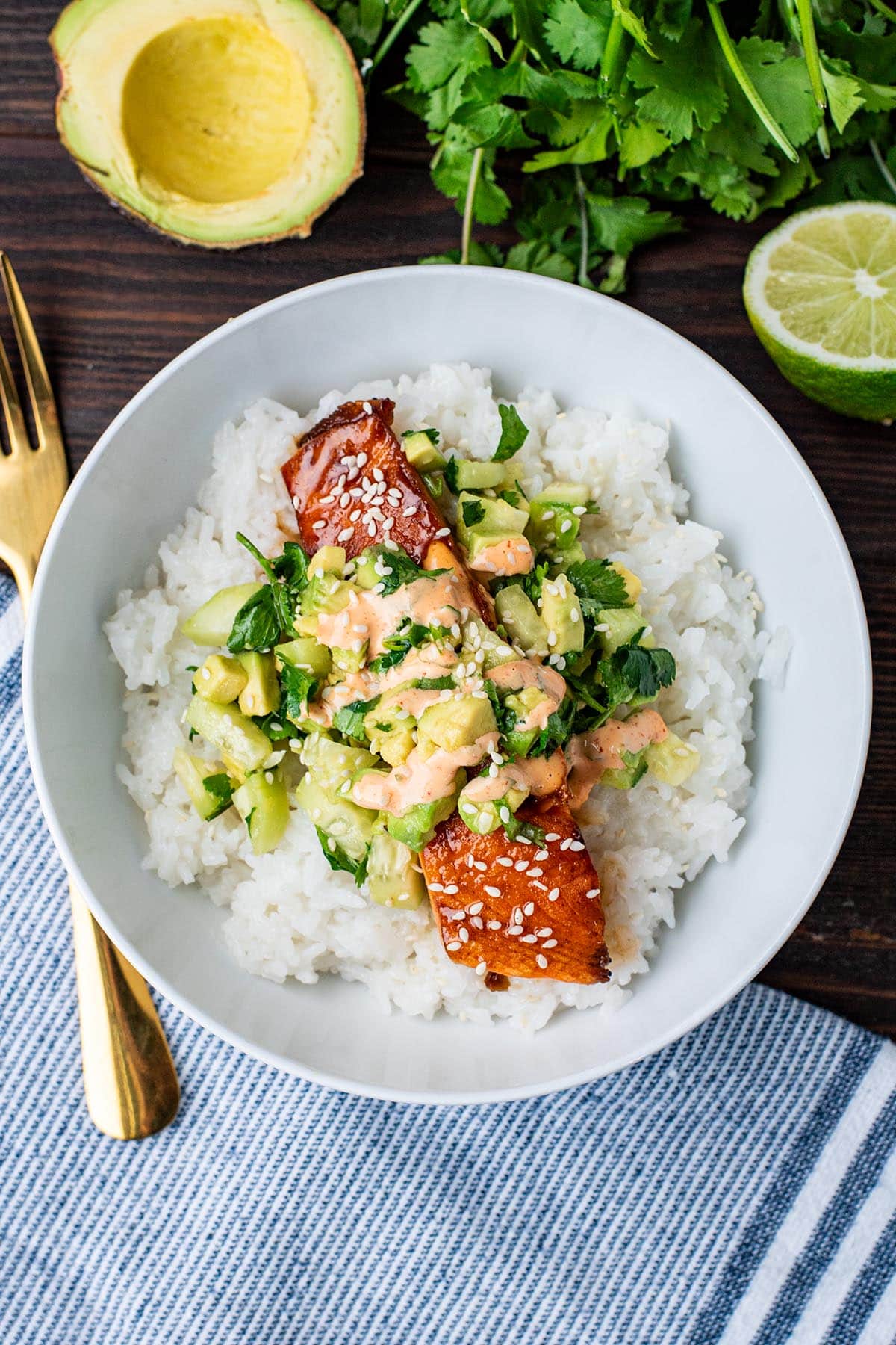 Honey glazed seared salmon in a white bowl served over white rice and topped with cucumber and avocado salad.