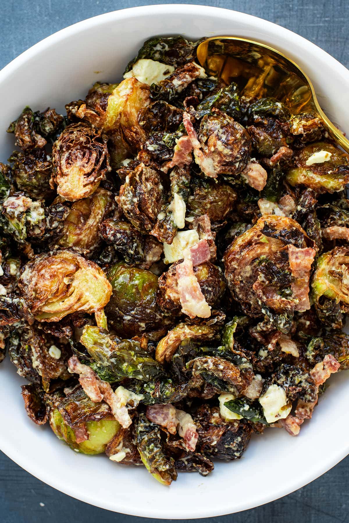 Golden fried Brussels sprouts in a bowl tossed with tahini sauce, feta cheese, and bacon chunks.
