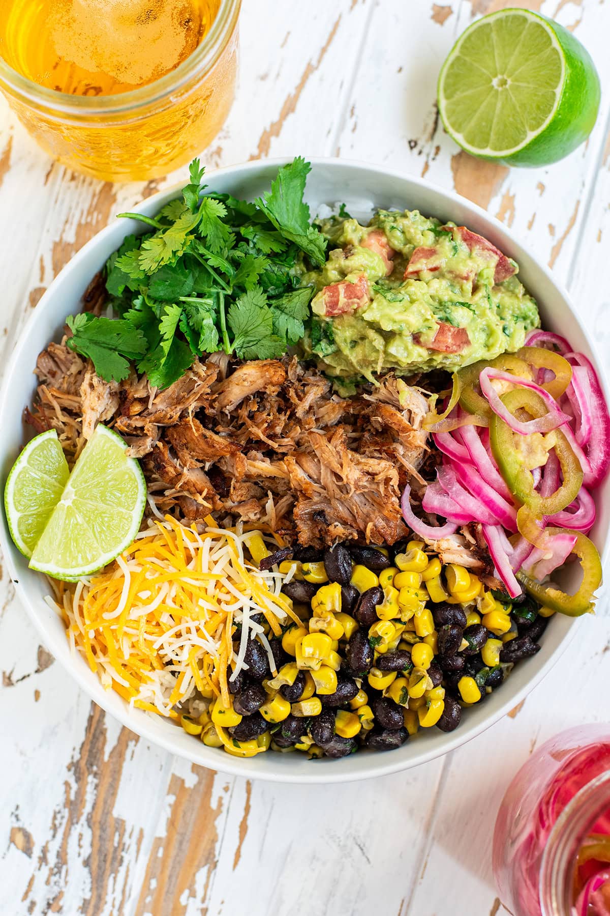 Carnitas taco bowl served over white rice topped with black beans/corn, pickled red onion, cheese, guacamole, and cilantro.