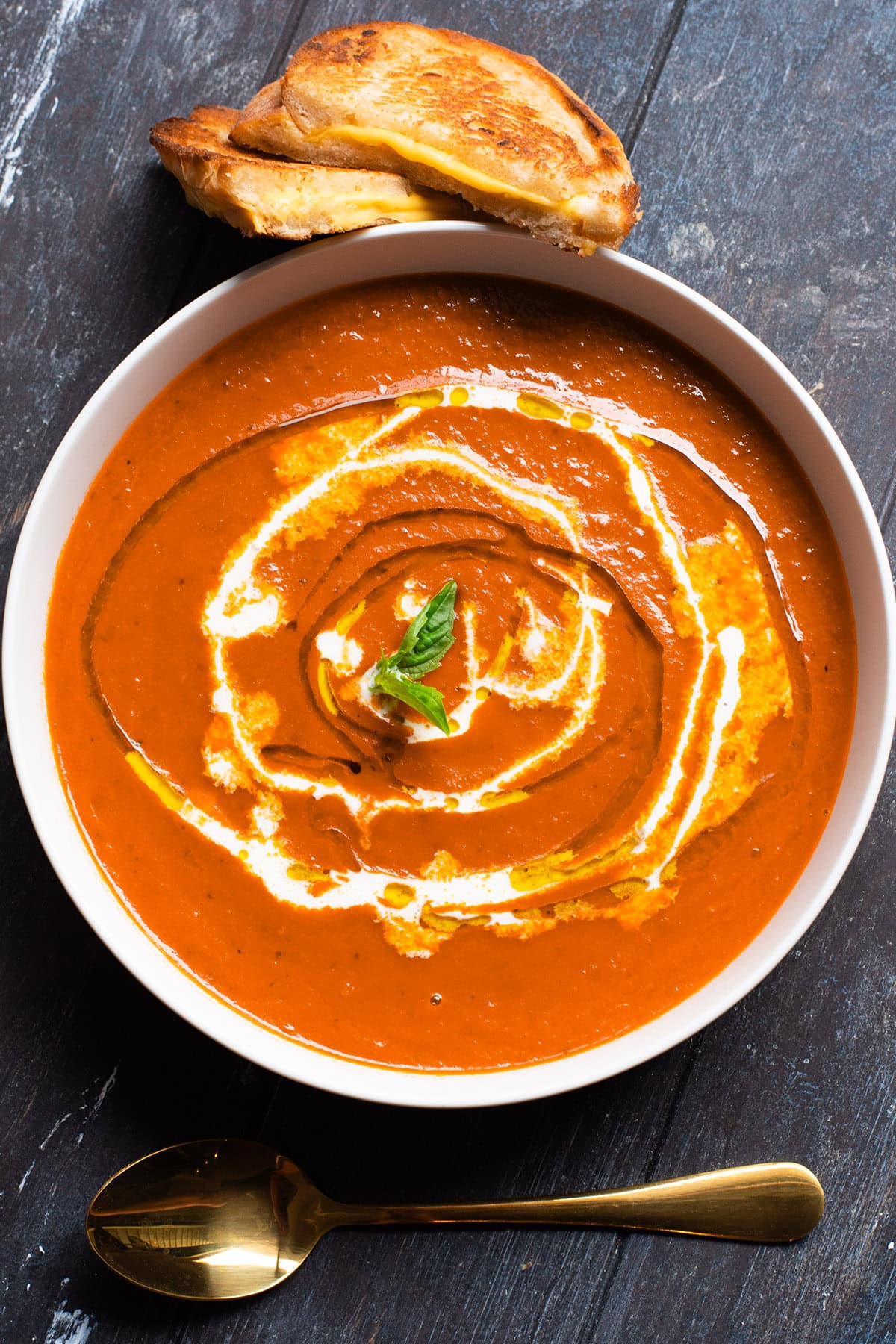 A bowl of creamy tomato basil soup topped with a drizzle of cream and olive oil.